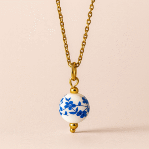 Charm de esfera estilo porcelana blanca con flores azules y detalles dorados en cadena dorada