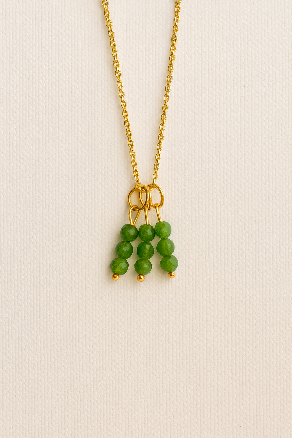 Charm con racimo de cuentas verdes facetadas y detalles dorados colgado en cadena dorada